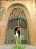 Vue de la porte d'entrée de droite, avec son arc parabolique et ses ornements en fer forgé.