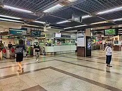 Personnes marchant au niveau du hall de la station, avec des faregates qui séparent les zones payées et non payées.