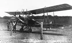 Photo en noir et blanc d'un biplan sur un air d'atterrissage avec deux hommes à côté.
