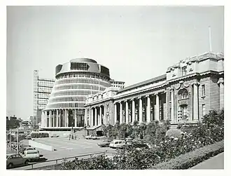 Photographie en noir et blanc d'un bâtiment moderne accolé à un bâtiment de style néoclassique, et encore en chantier.