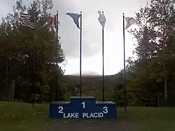 Un podium portant l'inscription « Lake Placid » devant cinq drapeaux.