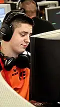 un jeune homme avec un maillot orange un micro-casque sur la tête et un second autour du cou.