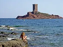 Jeune femme sur un rocher au bord de l'eau. Au loin une île surmontée d'une tour carrée.