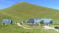 Deux bâtiments aux toits en taule bleutée sous un sommet couvert d'alpages.