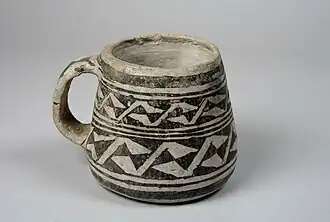 Tasse à anse légèrement conique, en céramique grise et noire, à fond plat.
