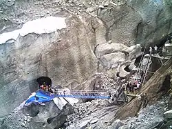 Passerelles menant à un cavité creusée dans un glacier en partie recouvert d'une bâche.