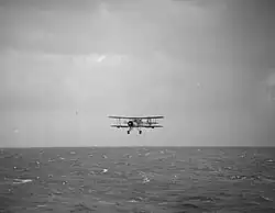 Photo en noir et blanc d'un avion biplan volant au-dessus de l'océan.