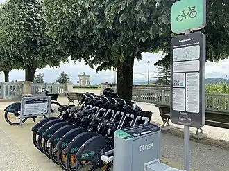 Une station remplie de vélos avec le belvédère de la place Royale en arrière-plan.