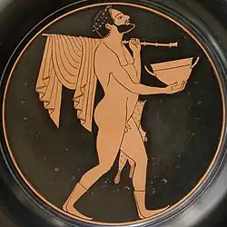 Comaste portant un skyphos, un bâton où s'enroule une draperie et un étui à flûtes, assiette à figures rouges, Paris, Bibliothèque nationale de France, Cabinet des médailles[9].
