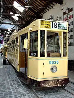Un tramway ancien, de couleur jaune pâle, exposé dans un musée, avec « girouette » bilingue indiquant les destinations en français et flamand.