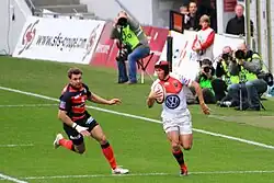 Joueur débordant sur le côté gauche du terrain, malgré l'arrivée d'un adversaire depuis son coté droit.