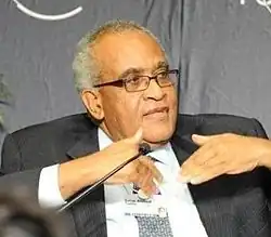 Photographie de Salim Ahmed Salim, représentant de l'Organisation de l'union africaine, un homme de couleur de peau basanée, aux cheveux blancs et portant des lunettes noires ainsi qu'un costume à la chemise blanche, veste noire et cravate décorée grise.