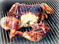 Gros plan des deux cuisses et du reste d'un poulet posé aplati sur un gril. La face visible de la viande est croustillante et porte les traces plus carbonisées des barres de métal du gril.