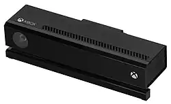 Photographie d'un appareil Kinect noir de la Xbox One sur fond blanc. On y voit dessus une caméra et les logo d'Xbox.