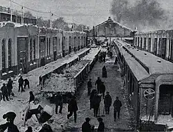 Plusieurs ouvriers se tiennent parmi des trains et des bâtiments, des pelles à la main