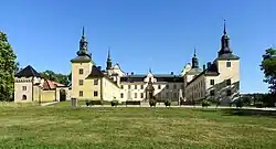 Grand château en U dans un parc vert.