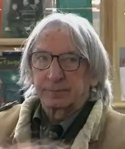 Homme âgé aux cheveux mi-longs portant une veste en mouton retourné.