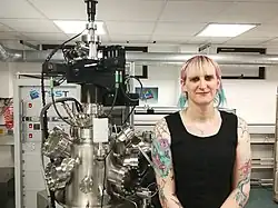 La docteure Clara Barker, debout dans son laboratoire, à côté d’un dispositif d’ablation à laser pulsé