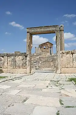 Vue de l'intérieur d'un édifice en ruine avec un temple muni de son fronton à l'arrière-plan