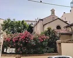 Dos du lieu de culte protestant, avec clocheton et haie fleurie.
