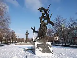Photographie d'une statue dans un parc enneigé, représentant un homme évanoui porté vers le ciel par des grues