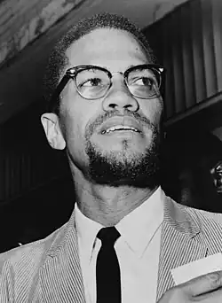 Photo en noir et blanc d'un homme noir portant un costume-cravate et des lunettes.