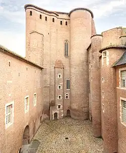 Photo couleur d'une haute tour de briques carrée flanquée de tourelles d'angle cylindriques et contreforts hémicylindriques.