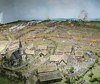À l'avant-plan, des soldats se battent parmi des bâtiments ; à l'arrière-plan, des soldats s'affrontent en rangs