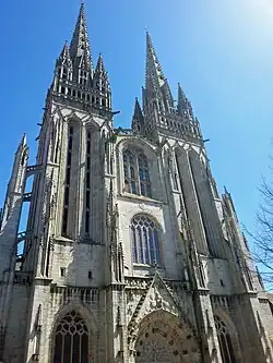 La façade ouest avec ses tours flanquées de baies géminées en plein cintre aux fenêtres entrecroisées de meneaux tréflés horizontaux, et surmontées d'une tribune.