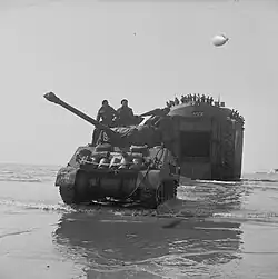 photographie en noir et blanc d’un char sur une plage avec un bateau à l’arrière plan