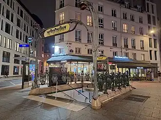 La même bouche d'accès à la station, vue à la nuit tombée.