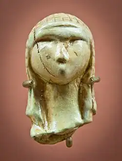 Tête de femme en ivoire vue de face, avec une coiffure qui descend jusqu'au cou et une balafre de dessiccation sur le côté droit.