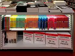 Meuble bas avec étagères dans le rayon histoire d'une librairie. Sur l'étagère du bas sont stockés des exemplaires de l'Histoire mondiale de la France.