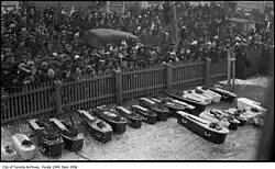 Photo noir et blanc d'une foule massée d'un côté d'une clôture en bois. De l'autre côté de la clôture, une vingtaine de cercueils (dont beaucoup adaptés à des corps d'enfants) reposent sur le sol.