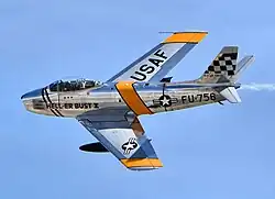 Photographie couleur d'un avion North American F-86 Sabre en vol se détachant sur un ciel bleu.