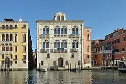 Au bord d'un canal, bâtiment de trois étages avec hautes fenêtes de style gothique aux second et troisième.