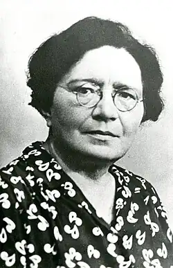 Femme aux lunettes rondes, portant une blouse à motif minimaliste.