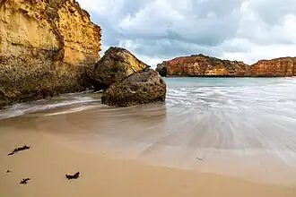 Sur une plage de sable, s'écoulant le long d'un rocher, une vague en se retirant dessine une courbe harmonieuse.
