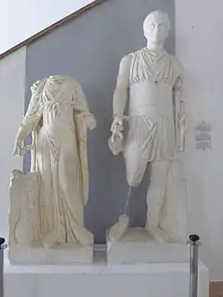 Vue de deux statues dont une femme qui n'a pas de tête et un homme qui porte une cruche et une sorte de bâton.