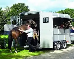 Un cheval monte dans une remorque les yeux bandés, guidé par un homme