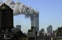 Photo des toits d'une grande ville. Au centre, un gigantesque panache de fumée grise s'élève de deux grands immeubles de bureaux.