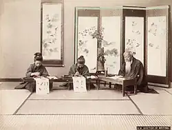 Professeur d'écriture, vers 1885. Photographie à l'albumine colorée à la main. Leçon de calligraphie (mise en scène).