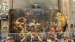 Un tableau de grande dimension est posé par terre sur un de ses longs côtés, dans une église.