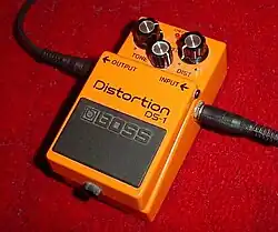 photographie d'une pédale d'effet orange avec deux jacks branchés de part et d'autre de la pédale.