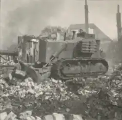 Photo noir et blanc d'un bulldozer roulant sur des ruines.
