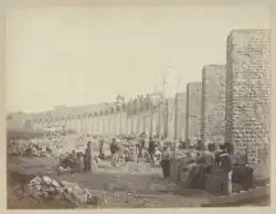 Photographie en sépia prise en contrebas du viaduc montrant des ouvriers du chantier, des piles sans arches et des arches en train d'être construites.