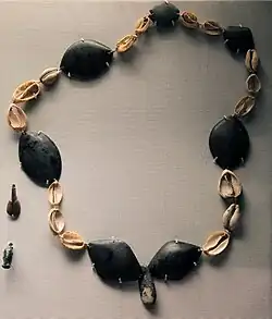 Collier de perles d'obsidienne et de coquillages cauris du golfe Persique anciennement colorés à l'ocre rouge, Tell Arpachiyah, période de Halaf. British Museum.