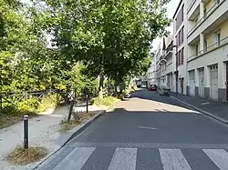 Vue de face d'une rue centrale longeant une rangée d'arbres à gauche et des immeubles d'habitation à droite