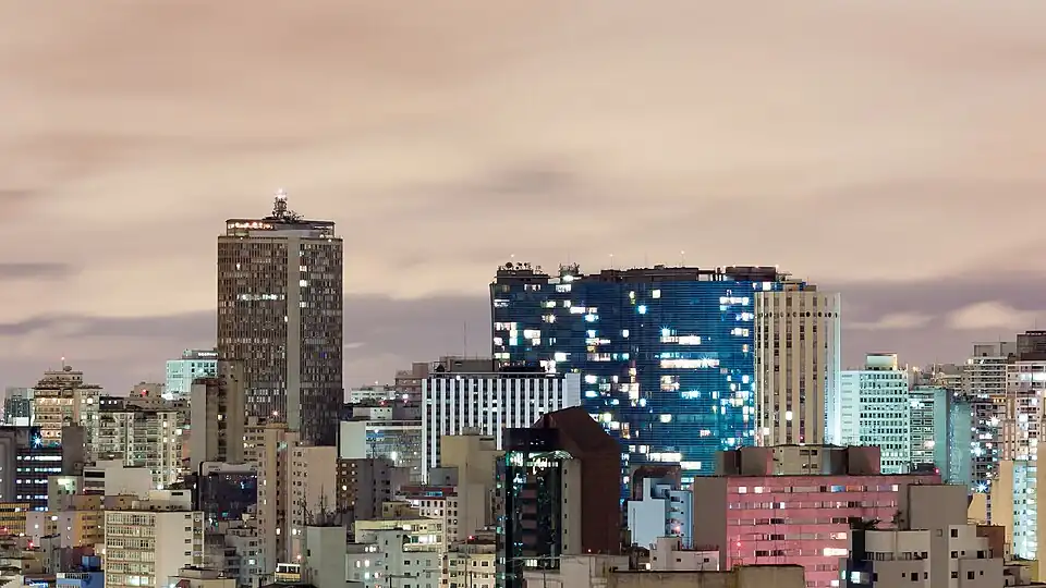 Photo de nuit où l'Edifício Itália et l'Edifício Copan émergent du paysage urbain. Des fenêtres sont éclairées de l'intérieur.