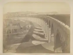 Photographie en sépia montrant le viaduc terminé, prise depuis la gauche de la balustrade de sécurité du pont qui fuit vers la gauche de l'image.
